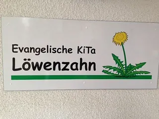 Schild mit Logo „Evangelische KiTa Löwenzahn“ und Pusteblume.
